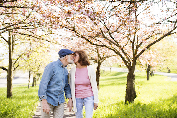 Beautiful senior couple in love on a walk outside, enjoying spring nature under blossoming trees. Man and woman kissing.