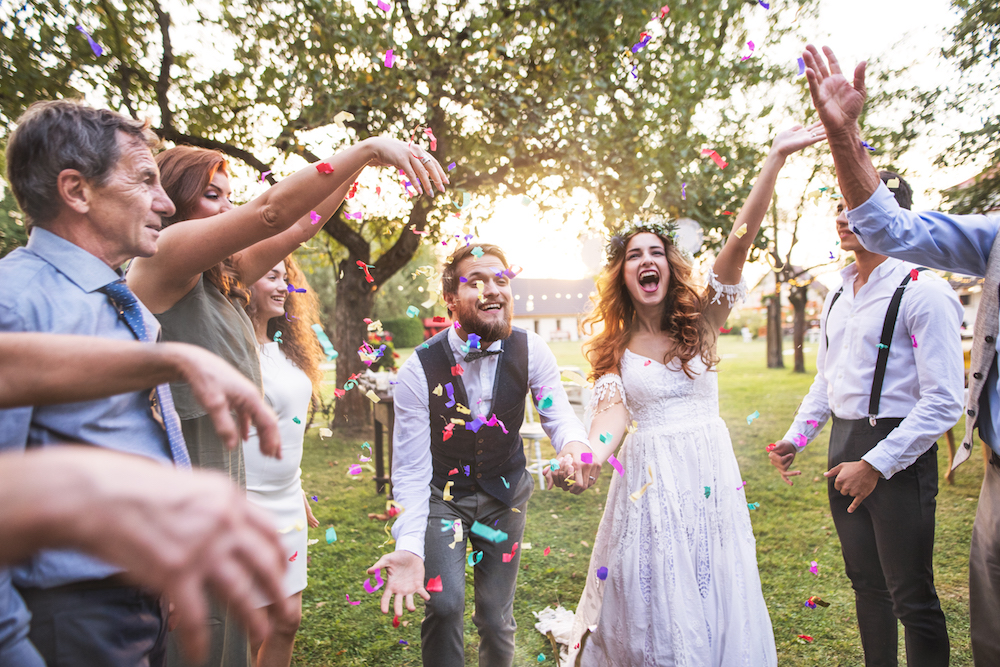 Bride, groom and their guests throwing confetti at the wedding reception outside in the backyard. Family celebration.